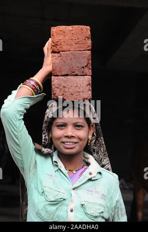 Pune; Maharashtra; Indien; Dez. 2015: Südost-Asien - Baustelle, indische Arbeiterin, die Ziegelsteine auf dem Kopf trägt; lächelnd. Stockfoto