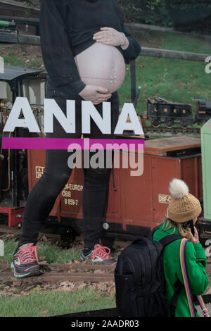 Eine junge Dame geht vorbei am großen Reklametafeln, Teil einer Serie von Porträts von Fotograf Lucy Alex Mac, dass schwangere Frauen an der West Smithfield Show, in der ehemaligen Smithfield Fleischmarkt, wartet auf die Zukunft Sanierung, am 20. November 2019, in Smithfield in der City von London, England. Als Teil des Museums des Londoner Pläne in Smithfield allgemeine Markt Gebäude, diese Fotografie zeigen zu bewegen feiert schwangere Bewohner von Waltham Forest. Die Kosten für den Umzug wird geschätzt, in der Region von 70 Millionen £, wenn Mittel erreicht werden können, würden bis 2021 abgeschlossen werden. Es wurde Stockfoto