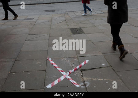 Beinen und Warnblinkschalter Klebeband gestreckt über einen gebrochenen Pflastersteine Platte auf einem clerkenwell Straße im Stadtteil Islington, am 20. November 2019 in London, England. Stockfoto