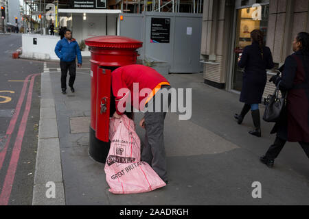 Ein Royal Mail Arbeiter und lehnt sich in ein Postfach ein Stapel von Briefen und Paketen zu leeren, am 20. November 2019, in der City von London, England. Stockfoto