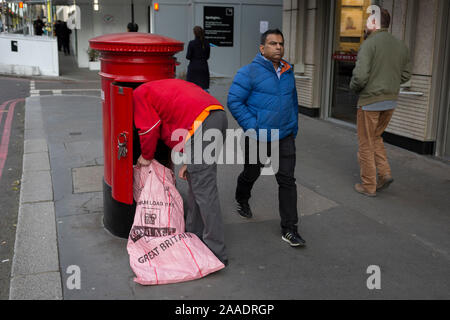 Ein Royal Mail Arbeiter und lehnt sich in ein Postfach ein Stapel von Briefen und Paketen zu leeren, am 20. November 2019, in der City von London, England. Stockfoto