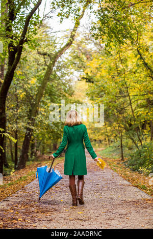 Frau mit Sonnenschirm und fallen Blätter beim Gehen in den Park. Stockfoto