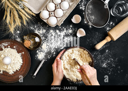 Weibliche Hände machen/Mixing Teig in brauner Schale auf Schwarzen Tisch, backen Vorbereitung close-up. Stockfoto