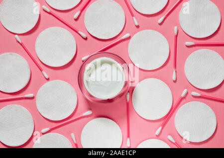Hygiene Produkte: Weiße runde Wattepads und Kunststoff Sticks für die Reinigung der Ohren liegen auf einem rosa Hintergrund nächste Creme zu Gesicht Stockfoto