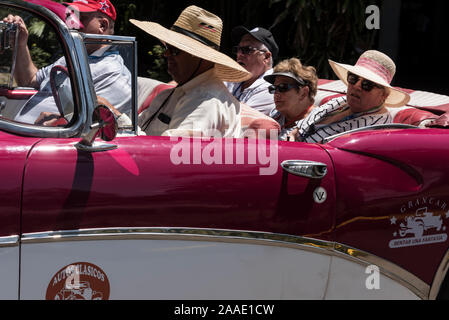 Eine Party von Touristen, die in einem amerikanischen Oldtimer für eine Tour durch Havanna auf Kuba Gefahren Wird, Viele der aufsehenerregenden Cabrio-Oldtimer-TA Stockfoto