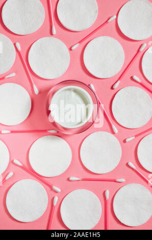 Hygiene Produkte: Weiße runde Wattepads und Kunststoff Sticks für die Reinigung der Ohren liegen auf einem rosa Hintergrund nächste Creme zu Gesicht Stockfoto