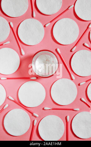 Hygiene Produkte: Weiße runde Wattepads und Kunststoff Sticks für die Reinigung der Ohren liegen auf einem rosa Hintergrund nächste Creme zu Gesicht Stockfoto