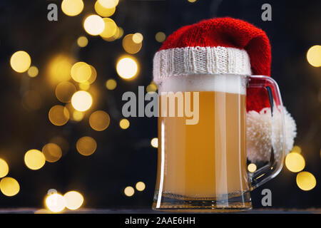 Weihnachten Bier, Ale-Becher in Santa Hut auf dunklem Hintergrund mit bokeh Girlande. Handwerk Bier Stockfoto