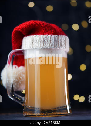 Weihnachten Bier, Ale-Becher in Santa Hut auf dunklem Hintergrund mit bokeh Girlande. Handwerk Bier Stockfoto