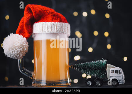 Weihnachten Bier, Ale-Becher in Santa Hut auf dunklem Hintergrund mit bokeh Girlande. Handwerk Bier Stockfoto