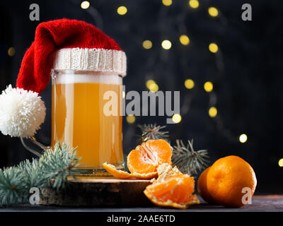 Weihnachten Ale Bierkrug in Santa Hut auf dunklem Hintergrund mit bokeh Girlande, Weihnachtsbaum, Zweige und Mandarinen. Das Handwerk Bier Stockfoto