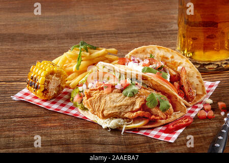 Chicken Fajitas mit gegrillten Zwiebeln und Paprika und mit Mehl Tortillas, Mais vom Grill und Pommes frites auf hölzernen Hintergrund Stockfoto