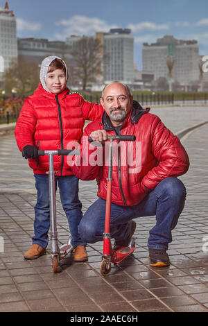 Eine Familie von zwei Menschen, sieben und 50 Jahre alt, entlang der Straße der Stadt in warme Kleidung gehen, bei kaltem Wetter. Vater und Sohn, in rot gekleidet, ja Stockfoto