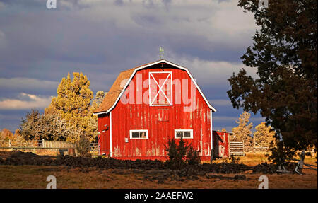 Eine alte rote hölzerne Scheune auf einem Bauernhof in der Nähe von Tumalo, Oregon, sitzt unter einem stürmischen Himmel. Stockfoto