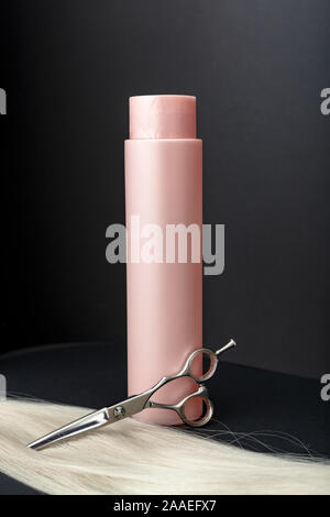 Shampoo für coloriertes Haar. Mockup Flasche Shampoo für blondes. Rosa Flasche kosmetisches Produkt, professionellen Friseur Schere und blonde Haare auf Schwarz Stockfoto