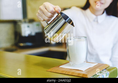 Der Prozess der Herstellung Kaffee Latte. Junge schöne Frau Barista im weißen Hemd Latte in einem Cafe, Coffee Shop, Bar. Glas mit doppelten Wänden. Stockfoto