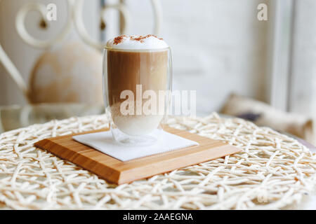 Hot Latte oder Cappuccino auf einem Tisch in einem Cafe in der Nähe der Fenster mit Copy space. Kaffee Latte mit Milch und Schokolade auf die Oberseite in ein doppelwandiger Stockfoto