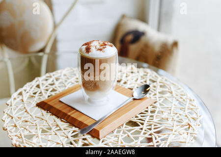 Hot Latte oder Cappuccino auf einem Tisch in einem Cafe in der Nähe der Fenster mit Copy space. Kaffee Latte mit Milch und Schokolade auf die Oberseite in ein doppelwandiger Stockfoto