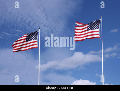 Zwei amerikanische Fahnen wehen im Wind gegen einen blauen Himmel mit dünnen Wolken. Stockfoto