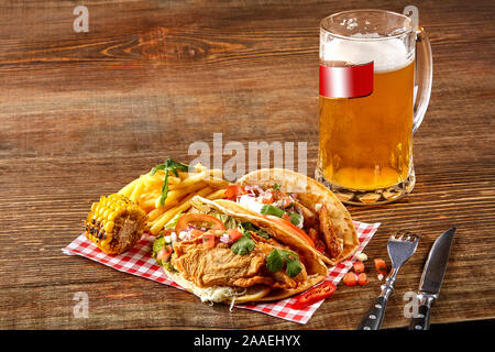 Erste mais Tortilla mit gegrilltem Hähnchen Filet, zweite mit Fischfilet, Soße und Bier auf hölzernen Tisch Stockfoto