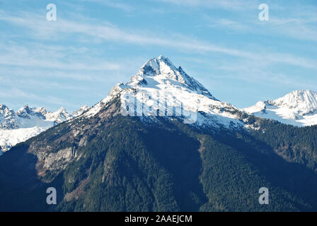 Eine der eindrucksvollen weißen schneebedeckten Gipfeln entlang der Tantalus Bergkette, mit dunkelgrünen Nadelbäumen, und einen klaren, blauen und weißen Himmel Stockfoto