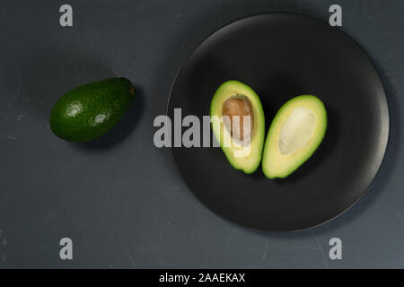 Frische, rohe Avocado in Scheiben geschnitten auf einer schwarzen Platte auf grauem Hintergrund Stockfoto