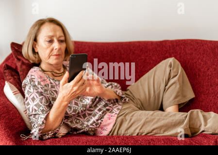 Elegante, reife Frau mit Smartphone, während auf dem Sofa sitzt. Stockfoto