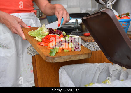 Detail einer weiblichen Hand Entsorgung der organischen Abfälle in einem geeigneten Behälter mit Küche im Hintergrund Stockfoto