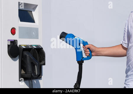 Der Fahrer hält Ladegerät für Elektroautos. Stromtankstelle. Umweltfreundliches Transportkonzept. Stockfoto