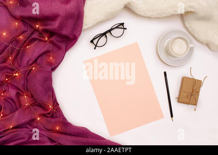 Eine Tasse Kaffee, schwarzen Brille, rosa Papier mit neuen Jahren Ziele. Schal und Weihnachtsbeleuchtung auf weißem Hintergrund. Stockfoto