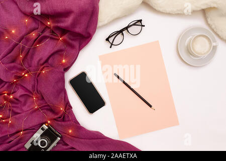 Eine Tasse Kaffee, schwarzer Smart, rosa Papier mit neuen Jahren Ziele. Schal und Weihnachtsbeleuchtung auf weißem Hintergrund. Stockfoto