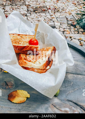Panini mit Schinken und Käse sandwich Papier auf einer hölzernen Tisch im Freien serviert. Street Market essen weg Konzept Stockfoto