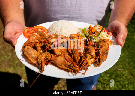 Ein Mann hält ein Schild mit Tiger Garnelen, Beilage und Salat. Stockfoto