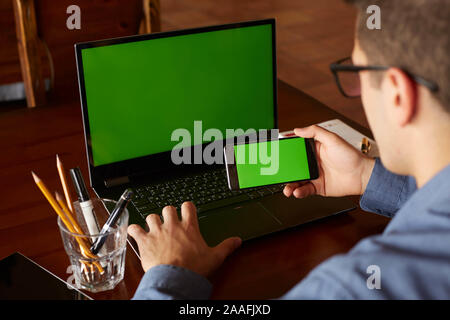 Rückansicht der Geschäftsmann mit Smartphone und Laptop eingeben im Amt. Green Screen mockup. Freelancer Arbeitsbereich. Mensch und Technik. Copyspace und Stockfoto