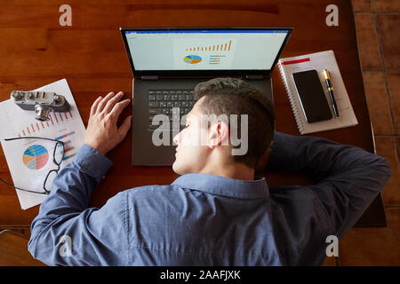 Blick von oben auf die müde, erschöpft, Geschäftsmann, schlafen auf Laptop Tastatur am Arbeitsplatz. Stattliche überarbeitet Freiberufler Mann liegen auf Holztisch und entspannt Stockfoto