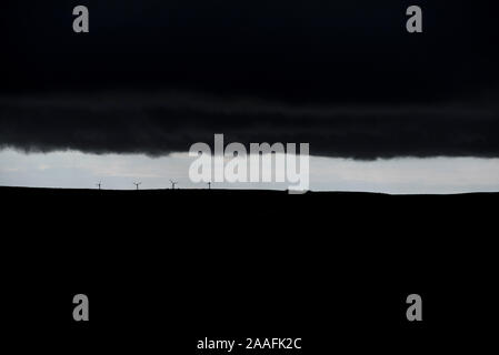 Ferner Windkraftanlagen auf der kanadischen Prärien Silhouette gegen einen dünnen Band der blauen Himmel mit Storm clouds Overhead Stockfoto