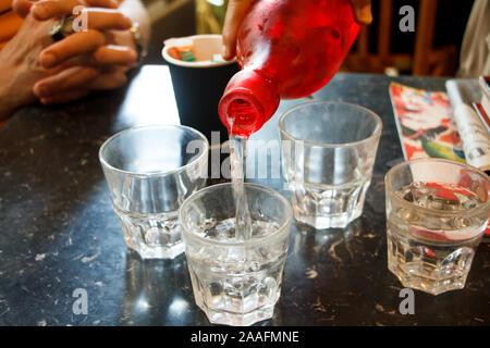 Close-up Hand Wasser ergießt sich aus einer roten Flasche in Glas Gläser auf einem Tisch im Restaurant Stockfoto