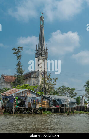 Cai, Mekong Delta, Vietnam - März 13, 2019: Entlang der Kinh 28 Kanal. Katholische Kirche, Nha Tho, mit grauen Stein lange schlanke clock Spire und Madonna st Stockfoto