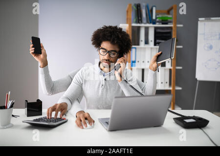 Lächelnde junge Unternehmer tun Multitasking am Arbeitsplatz Stockfoto