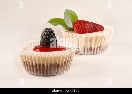 Hausgemachter Käsekuchen und hausgemachte Erdbeersauce von Erdbeeren, Brombeeren und Himbeeren auf weißem Hintergrund begleitet. Stockfoto
