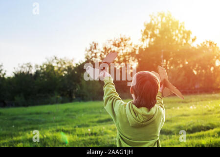 Kind startet Papierflieger. Junge, grüne Jacke über Feld bei Sonnenuntergang läuft. Glückliche Kindheit. Zu Fuß auf der Straße ohne ein Telefon. Stockfoto