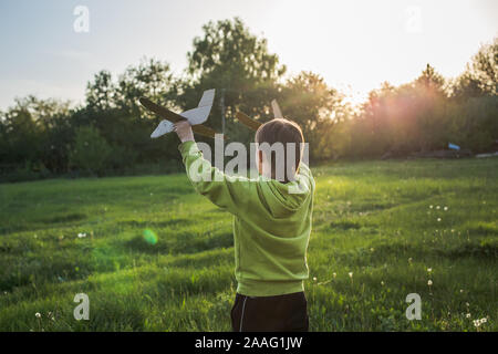 Kind startet Spielflugzeug. Flugreisen. Junge Spaziergänge im Dorf über den Schlag bei Sonnenuntergang. Stockfoto