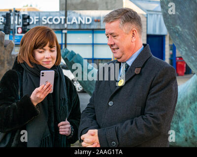 Loanhead, Midlothian, Schottland, Vereinigtes Königreich: 2019 Bundestagswahlkampf. SNP Stellvertretende Vorsitzende Keith Brown MSP mit partei Mitglied am Telefon Stockfoto