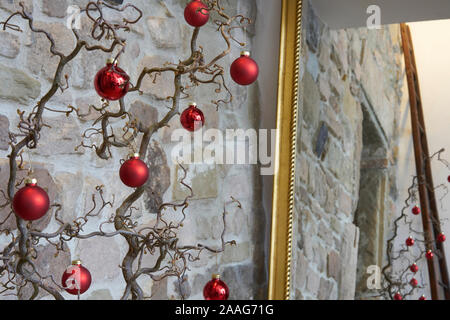 Roten Weihnachtskugeln an einem Zweig vor einer Mauer aus Stein, in einen Spiegel mit goldenem Rahmen, loft apartment Stockfoto