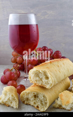 Frisch gebackenes Baguette, lecker Rotwein und frischem roten Trauben auf einem grauen Stein Hintergrund. Stockfoto