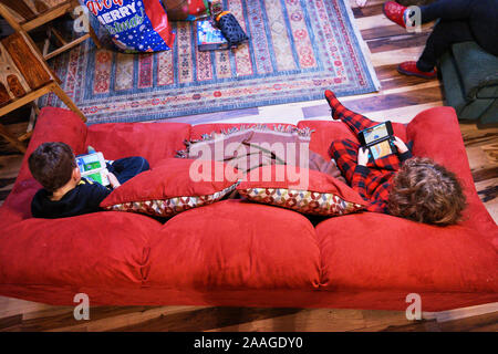 Zwei Jungs sitzen auf einem roten Sofa und spielen Handheld Videospiele während der Weihnachtsferien in Willits, Kalifornien. Stockfoto