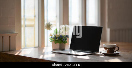 Komfortabler Arbeitsplatz mit Laptop, Kaffee Tasse und Baum Topf auf Holztisch neben Windows Stockfoto
