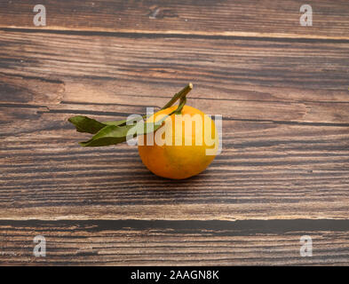 Eine gelbe Tangerine auf einem Zweig mit grünen Blättern auf einer hölzernen Hintergrund. Herbst Ernte. Die moderne Landwirtschaft. Für einen süßen Leckereien Stockfoto