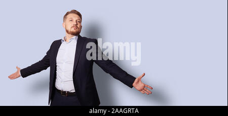 Gut aussehender bärtiger Mann mit offenen Armen in einem Anzug ohne Krawatte. Studio Portrait über grau blau Hintergrund. Stockfoto