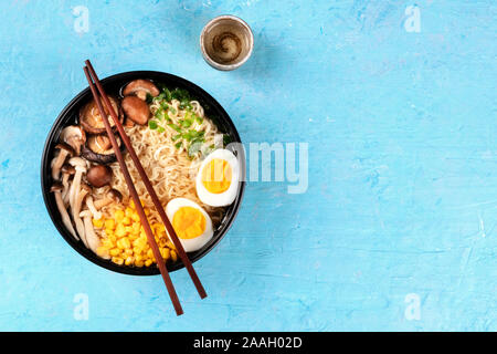 Ramen. Soba Nudeln mit gekochten Eiern, Shiitake-pilze, und Gemüse, Top Shot auf einem blauen Hintergrund mit Stäbchen, eine Tasse Sake und Copyspace Stockfoto